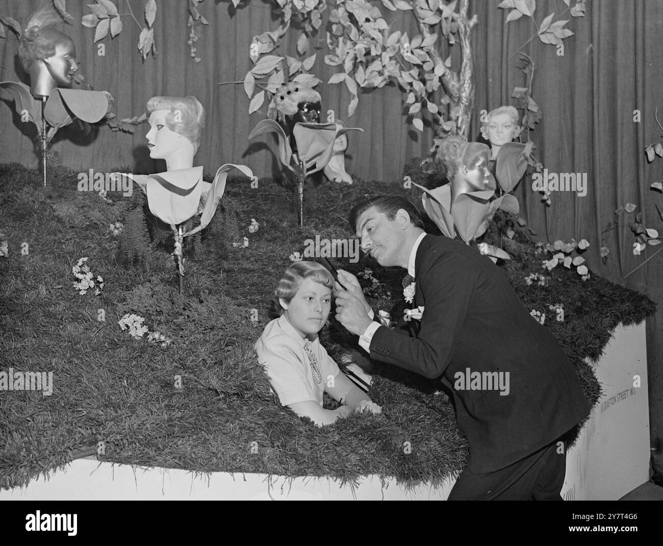 TRA LA NATURA MORTA M.. Raymond, famoso parrucchiere londinese, si vede adattare l'acconciatura del suo modello di vita reale stellare, piantato tra i modelli di natura morta nel suo stand alla mostra di parrucchiere Beaux Arts di Londra, oggi. 8 giugno 1949 Foto Stock