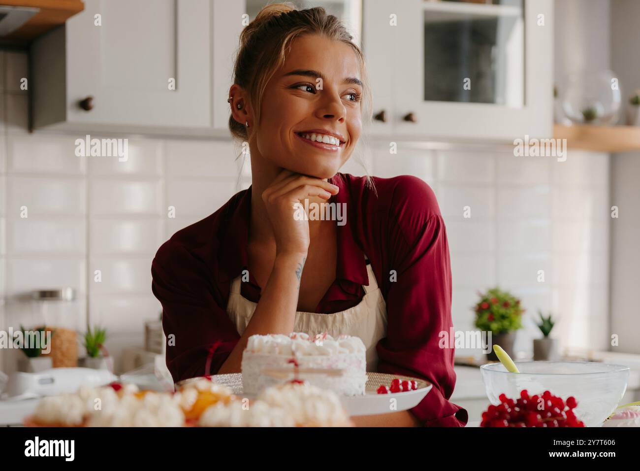 Giovane pasticcera che pensa a nuove idee creative mentre si appoggia a tavola con il dolce Foto Stock