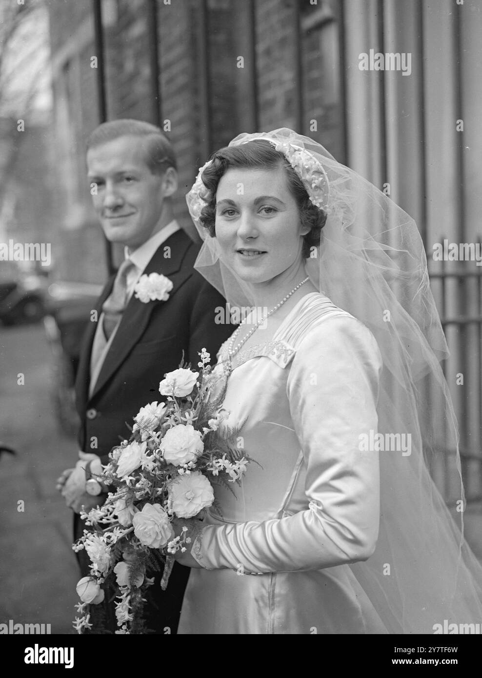 LA FIGLIA DEL CHIRURGO SPOSA la signorina Elizabeth Griffiths, figlia di 23 anni del chirurgo di Harley Street Sir Hugh Griffiths, per il quale ha lavorato come segretaria, era sposata con Mr Henry Padfield , 26 anni membro dei Lloyd's nella chiesa Santa della Trinità, Brompton, Londra oggi. L'IMMAGINE MOSTRA: La sposa e lo sposo che lasciano la chiesa. Il velo in tulle luminoso è tenuto da un cappuccio alato di raso , cucito con perle e fiori d'arancio. Il suo abito classico è di raso duchessa bianco con corpetto ricamato perla, porta un bouquet doccia . 4 febbraio 1950 Foto Stock