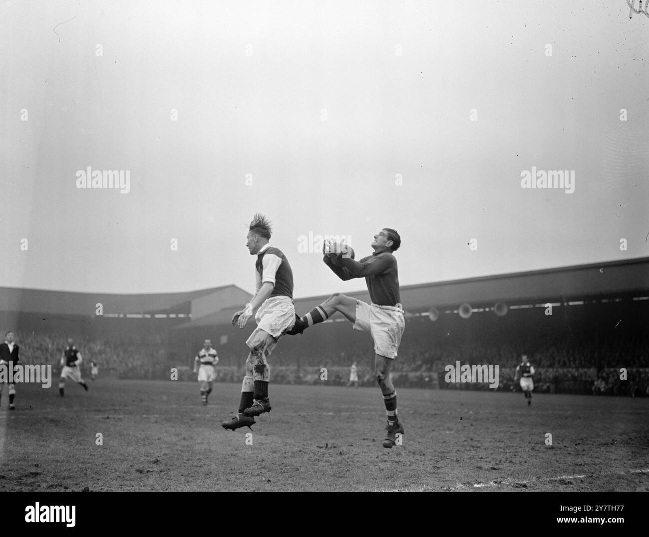 AIUTANDOLO PER STRADA! Prendendo la palla al sicuro tra le sue braccia, Reg Allan, portiere del Queens Park Ranger, dà l'illusione che stia usando la punta della sua scarpa per fornire a MauriceTadman, Plymouth Argyle centro avanti, un campo di sollevamento durante la partita di seconda divisione a Loftus Road Ground, Londra. 22 ottobre 1949 Foto Stock