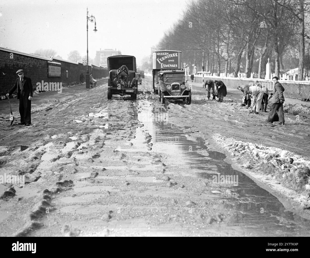 Ghiaccio, neve e acqua pura che si combinano per creare una rotta ad ostacoli per il traffico in Wellington Street, St John's Wood, Londra. Gli uomini sulla destra sono al lavoro sul ghiaccio con picchetti e fornelli 8 marzo 1947 Foto Stock