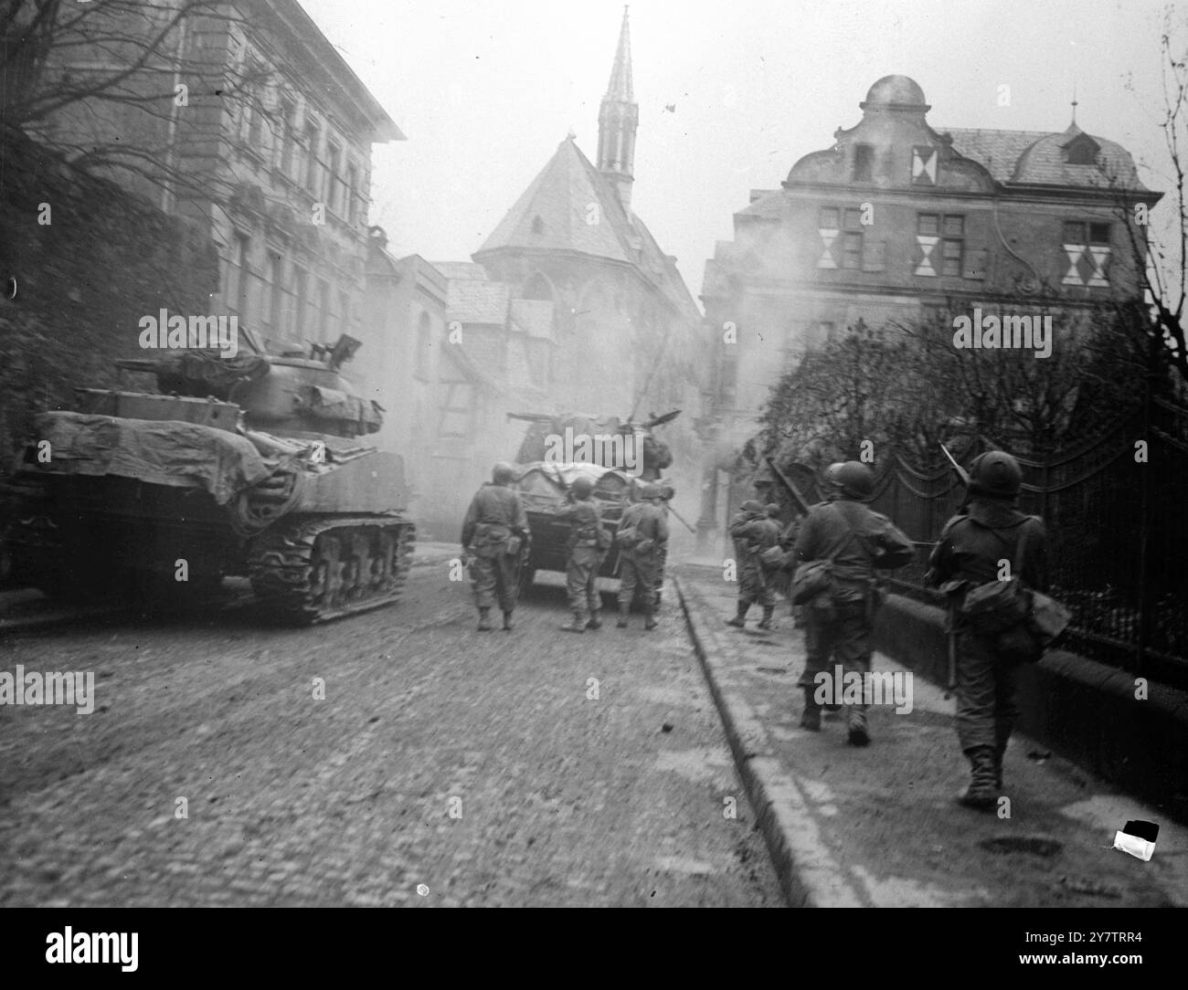 Street Fighting in GermanyFotografia: Fanteria seguite i carri armati della 11a Divisione corazzata, la 3a Armata americana ad Andernach, Germania. Un cecchino sta sparando alle truppe dall'edificio a sinistra , e un fanteria dietro il carro armato principale lo ha avvistato il 14 marzo 1945 Foto Stock