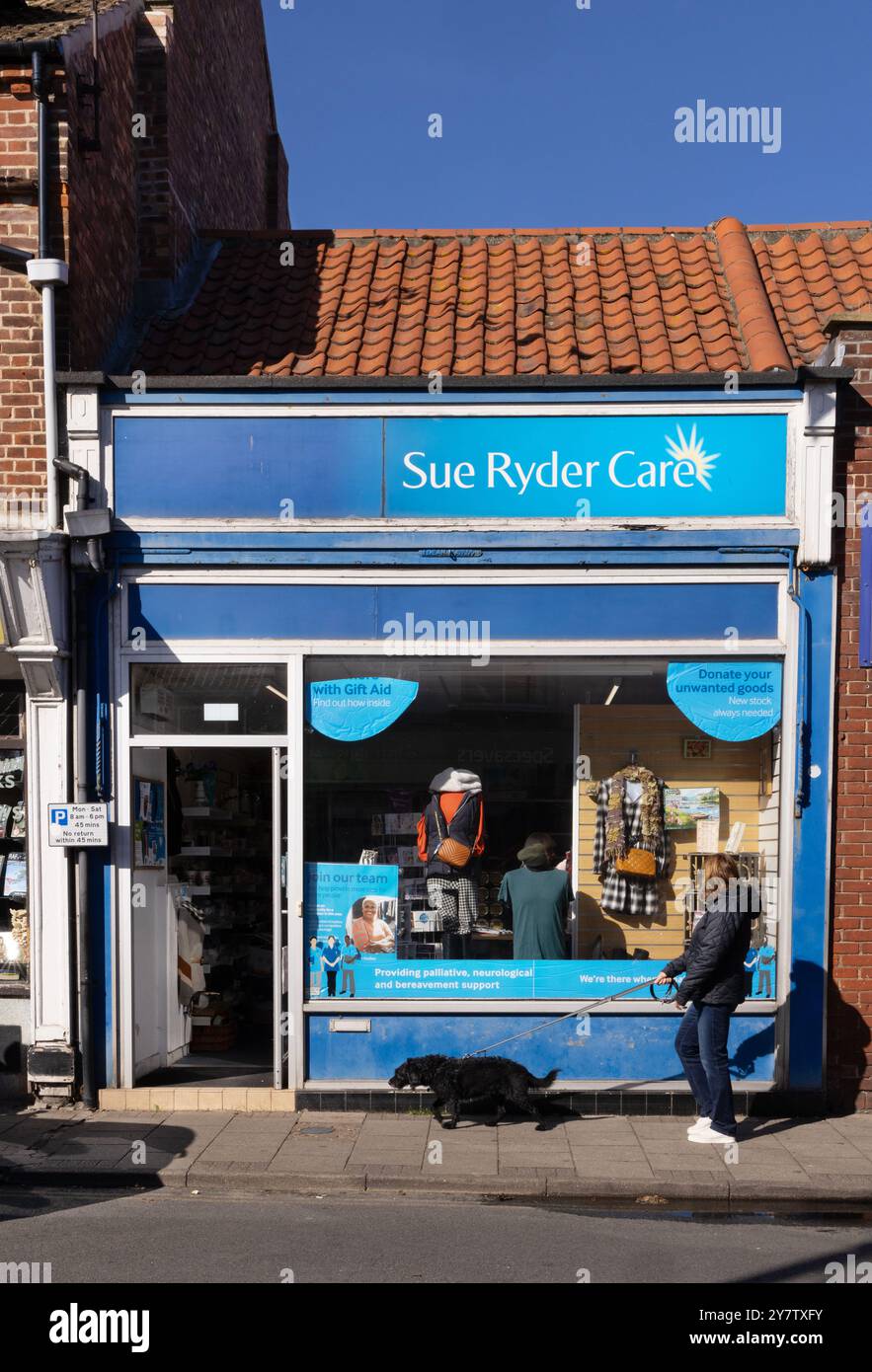 Una donna che passa accanto a un negozio di beneficenza sue Ryder Care; Sheringham, Norfolk Regno Unito. Negozi di beneficenza nel Regno Unito e nel Regno Unito Foto Stock