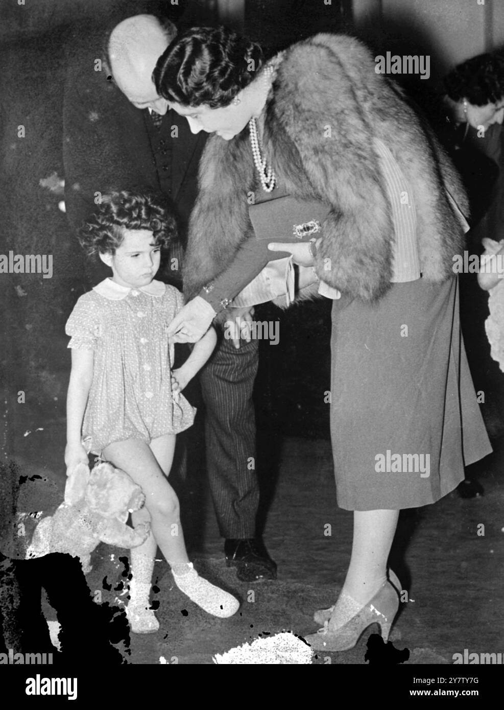 LA REGINA ISPEZIONA I VESTITI DEI BAMBINI mentre si trovava a Buckingham Palace, sua Maestà la Regina ispezionò copie di abiti di cotone per bambini che sono stati esposti a New York, e che sono stati inviati dalla Gran Bretagna negli Stati Uniti, per portare più soldi per lo sforzo bellico. Una mostra sulle stesse linee si terrà a Londra, a partire dalla prossima settimana. Spettacoli fotografici: Georgina Goddard, di quattro anni, "si erge" mentre sua Maestà ispeziona e sente la consistenza del cotone che indossa il bambino. 27 febbraio 1941 Foto Stock