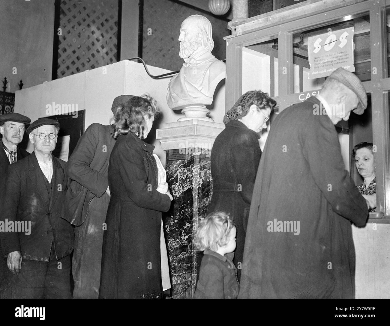 LONDINESI PRANZO CON GLI DEI: PASTI DA MUSEO A PREZZI POPOLARI ristoranti britannici, aperti dal Londoners' Meals Service per fornire buon cibo a prezzi minimi, sono apparsi quasi ovunque a Londra, da Park Lane a Putney, durante la guerra. Il più strano è al Bethnal Green Museum, nell'East End, dove ogni giorno possono essere serviti 1000 pranzi caldi. I clienti pagano dieci pence o uno scellino nel salone, in uno stand accanto a un busto di Garibaldi, il patriota italiano, e fanno il loro pasto presso un banco di servizio, portandolo davanti a un busto di Oliver Cromwell, Lord Protettore del commonwealth, al c Foto Stock