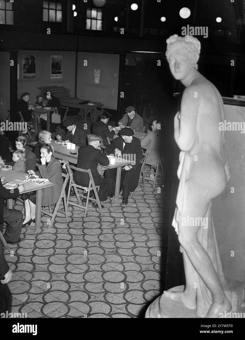LONDINESI PRANZO CON GLI DEI: PASTI DA MUSEO A PREZZI POPOLARI ristoranti britannici, aperti dal Londoners' Meals Service per fornire buon cibo a prezzi minimi, sono apparsi quasi ovunque a Londra, da Park Lane a Putney, durante la guerra. Il più strano è al Bethnal Green Museum, nell'East End, dove ogni giorno possono essere serviti 1000 pranzi caldi. I clienti pagano dieci pence o uno scellino nel salone, in uno stand accanto a un busto di Garibaldi, il patriota italiano, e fanno il loro pasto presso un banco di servizio, portandolo davanti a un busto di Oliver Cromwell, Lord Protettore del commonwealth, al c Foto Stock