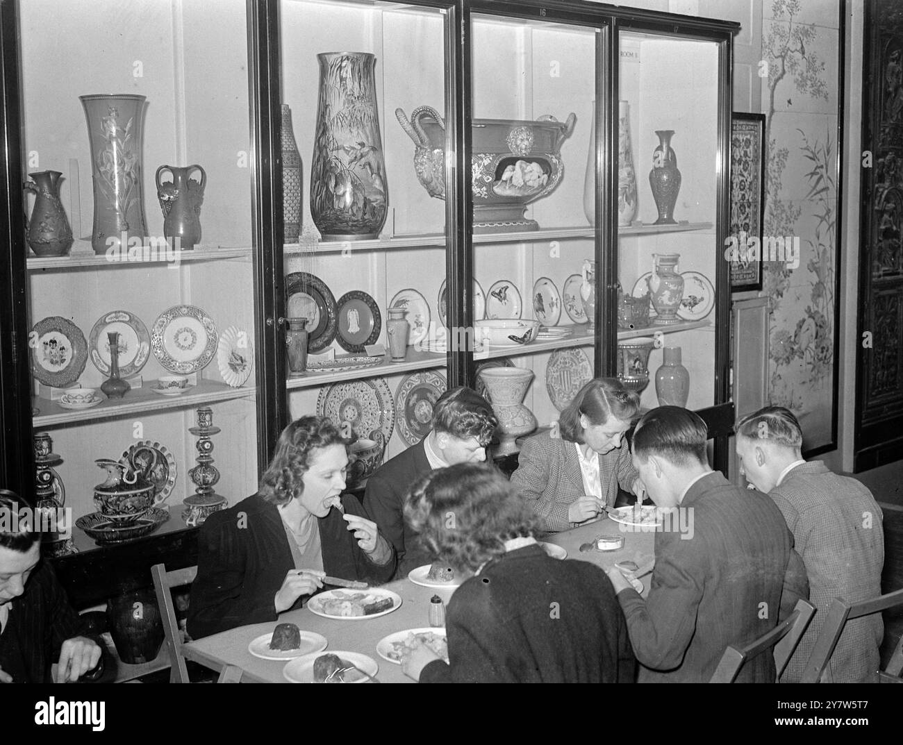 LONDINESI PRANZO CON GLI DEI: PASTI DA MUSEO A PREZZI POPOLARI ristoranti britannici, aperti dal Londoners' Meals Service per fornire buon cibo a prezzi minimi, sono apparsi quasi ovunque a Londra, da Park Lane a Putney, durante la guerra. Il più strano è al Bethnal Green Museum, nell'East End, dove ogni giorno possono essere serviti 1000 pranzi caldi. I clienti pagano dieci pence o uno scellino nel salone, in uno stand accanto a un busto di Garibaldi, il patriota italiano, e fanno il loro pasto presso un banco di servizio, portandolo davanti a un busto di Oliver Cromwell, Lord Protettore del commonwealth, al c Foto Stock