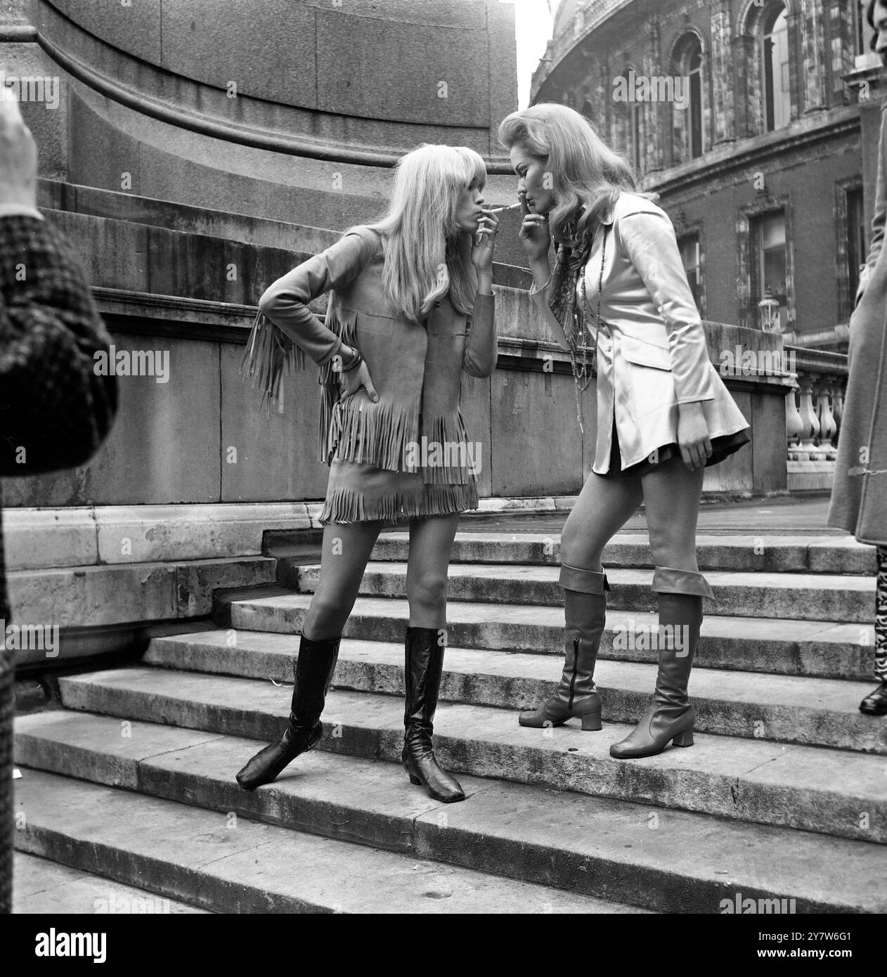 Jayne Hodge (a destra) e Amanda Lear (a sinistra) illuminano le loro sigarette l'una dall'altra, come appaiono oggi nei costumi che indosseranno ciascuno al Christmas Party 1968 di Ossie Clark e Alice Pollock, alla Royal Albert Hall (vista in sottofondo) a Londra il 19 dicembre 1968. Si esibiranno molti dei migliori musicisti pop, tra cui Julie Driscoll, Brian Auger e The Trinity, e Bonzo Dog Do Dah Band. I proventi vanno al Fondo Save the Children.15 dicembre 1968 Foto Stock