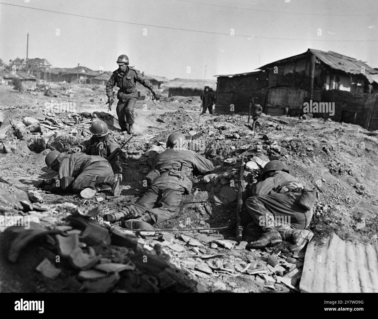 Corsa a piedi con morte in guerra Seared Korea letteralmente in corsa tra i proiettili un fanteria alleato , schiacciato per unirsi ai suoi compagni di squadra di combattimento nella scarsa copertura offerta dalle macerie di una piccola città coreana , mentre il loro gruppo è bloccato dal fuoco di armi leggere . Un altro soldato si ferma all'angolo di un edificio abbandonato prima di rischiare il guanto di piombo rosso . Le truppe delle Nazioni Unite sono state duramente pressate dalle forze cinesi superiori , che hanno subito pesanti perdite , ma non sono riuscite a intrappolare le truppe alleate . 27 aprile 1951 Foto Stock