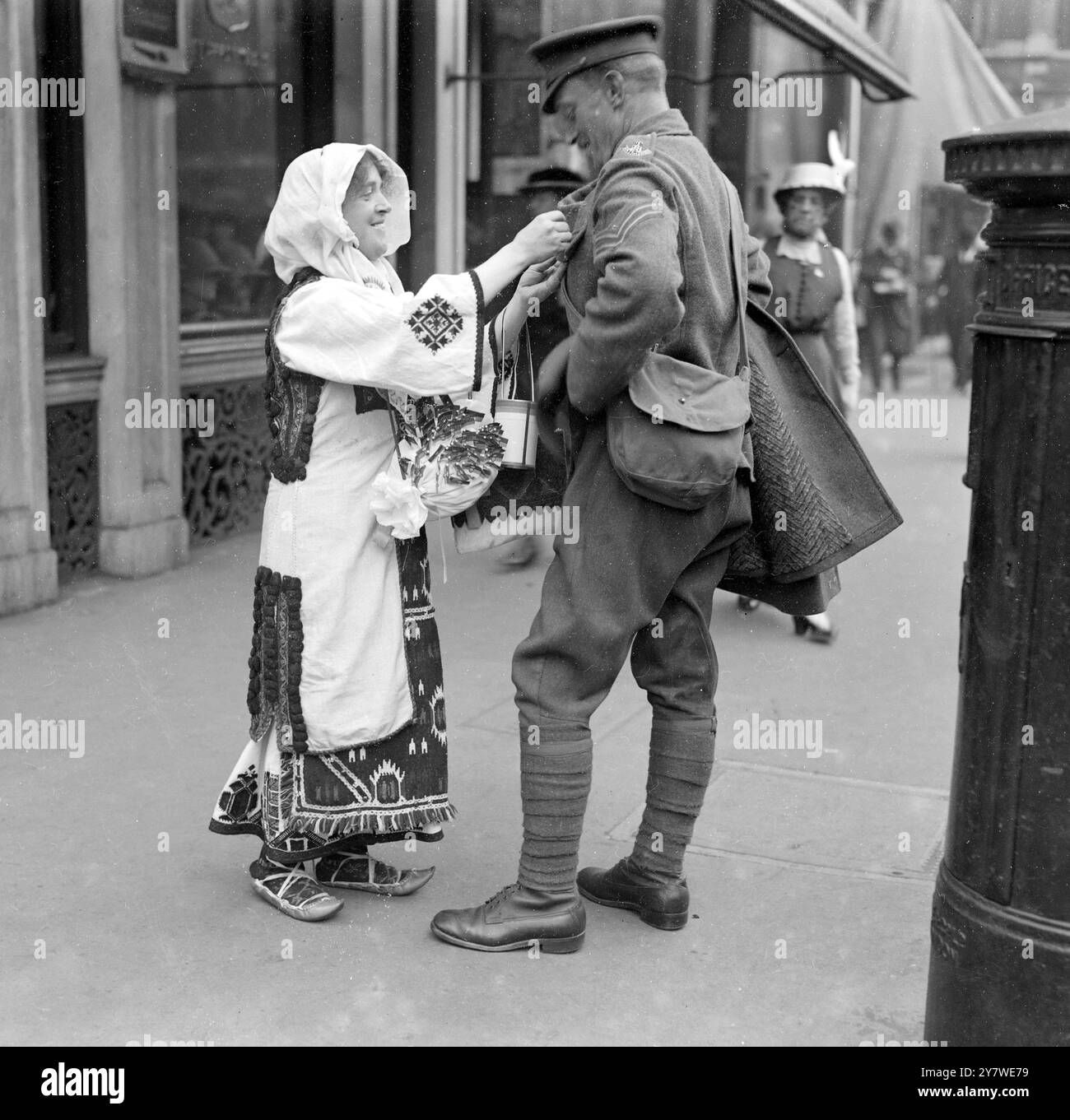 Una signora vestita in costume serbo infila una bandiera su un soldato mentre raccoglie per il Fondo per la giornata della bandiera serba di Londra . anni '1910 Foto Stock