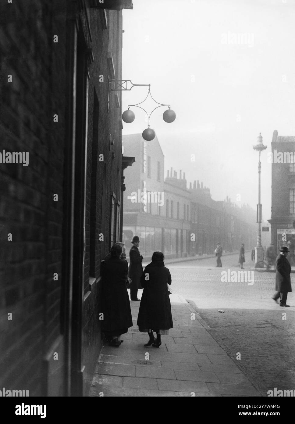 Le donne aspettano sotto il segno delle tre palle per aprire il banco dei pegni il lunedì mattina a Stepney , East London - 1933 ©TopFoto Foto Stock