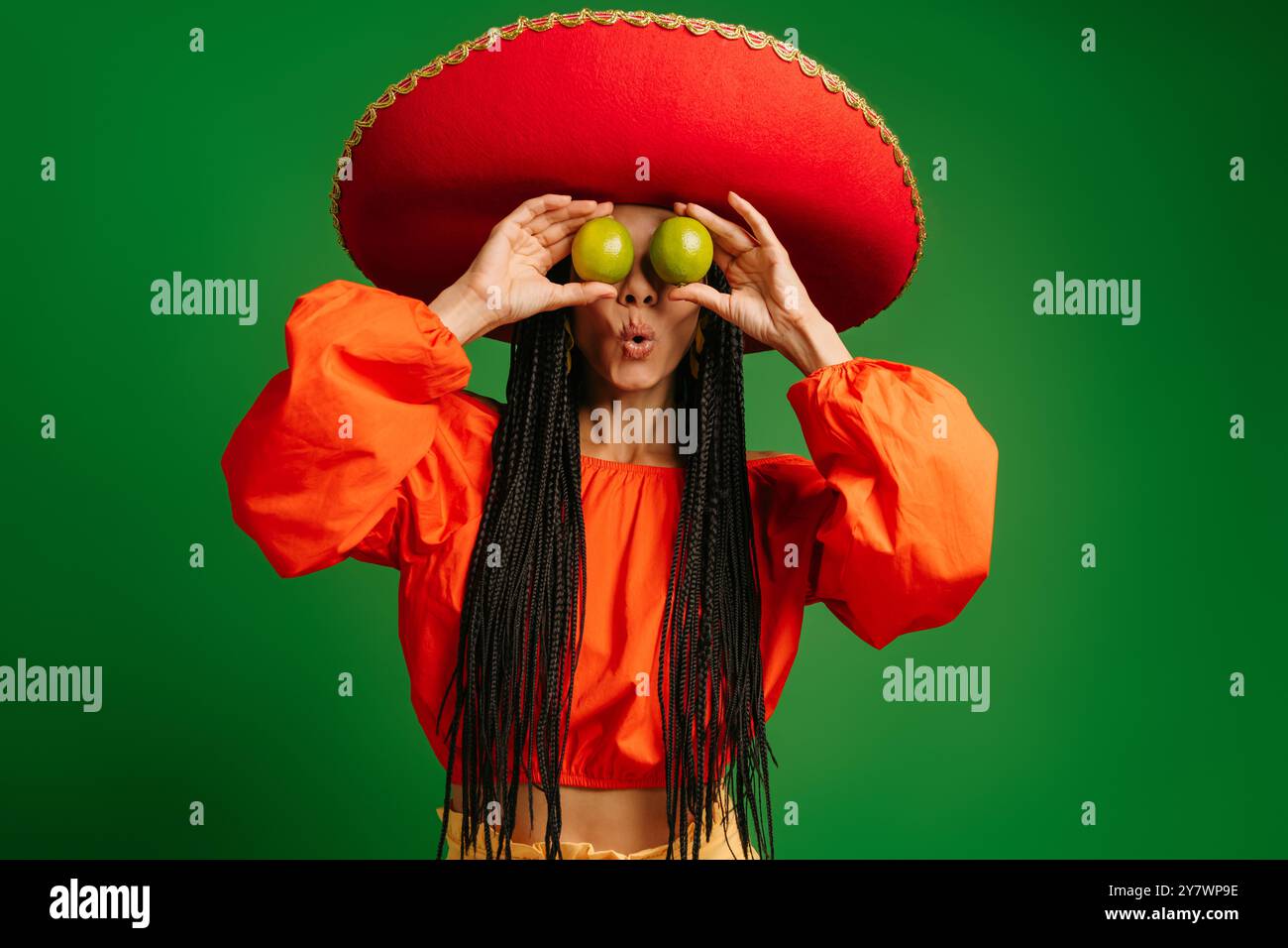 Sorpresa la giovane donna messicana di Sombrero che copre gli occhi con un limes fresco su sfondo verde Foto Stock Sorpresa la giovane donna messicana di Sombrero che copre gli occhi con un limes fresco su sfondo verde Foto Stock