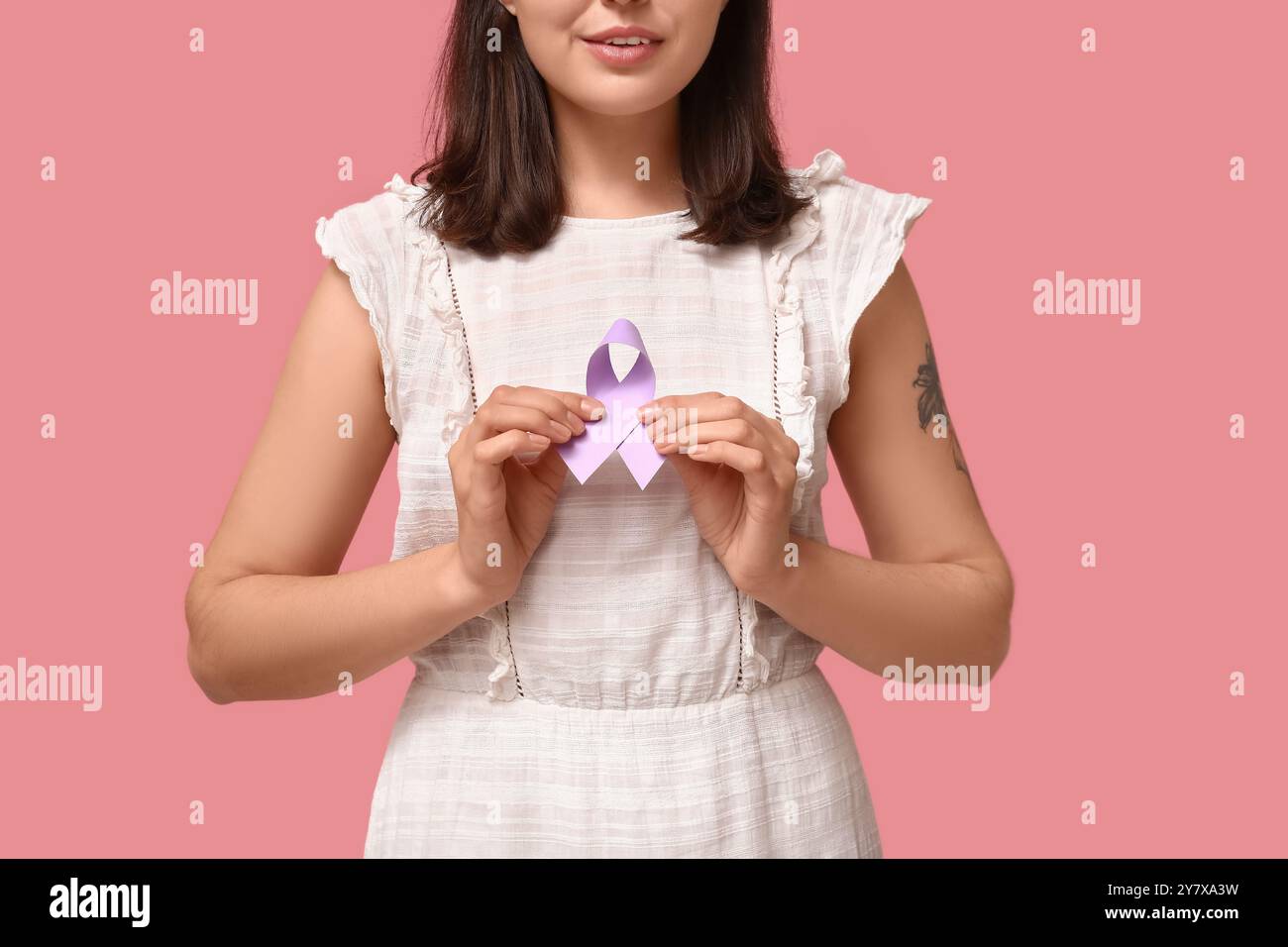 Donna con nastro viola chiaro su sfondo rosa. Concetto di consapevolezza del cancro testicolare Foto Stock