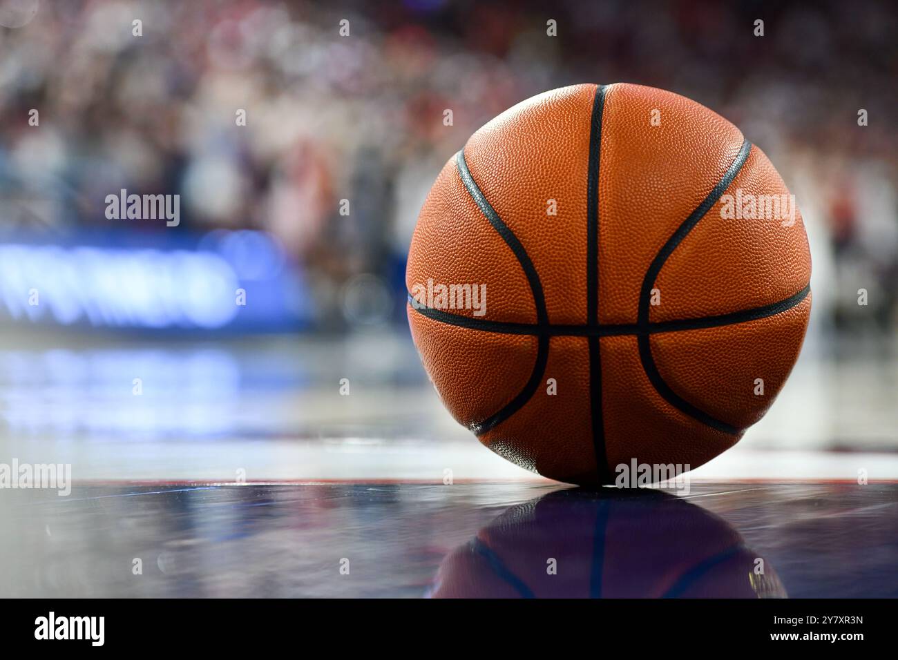 Primo piano di un pallacanestro su un elegante campo di Hardwood, sotto le luci dell'arena, catturando la tensione e l'energia del gioco con ombre sottili Foto Stock