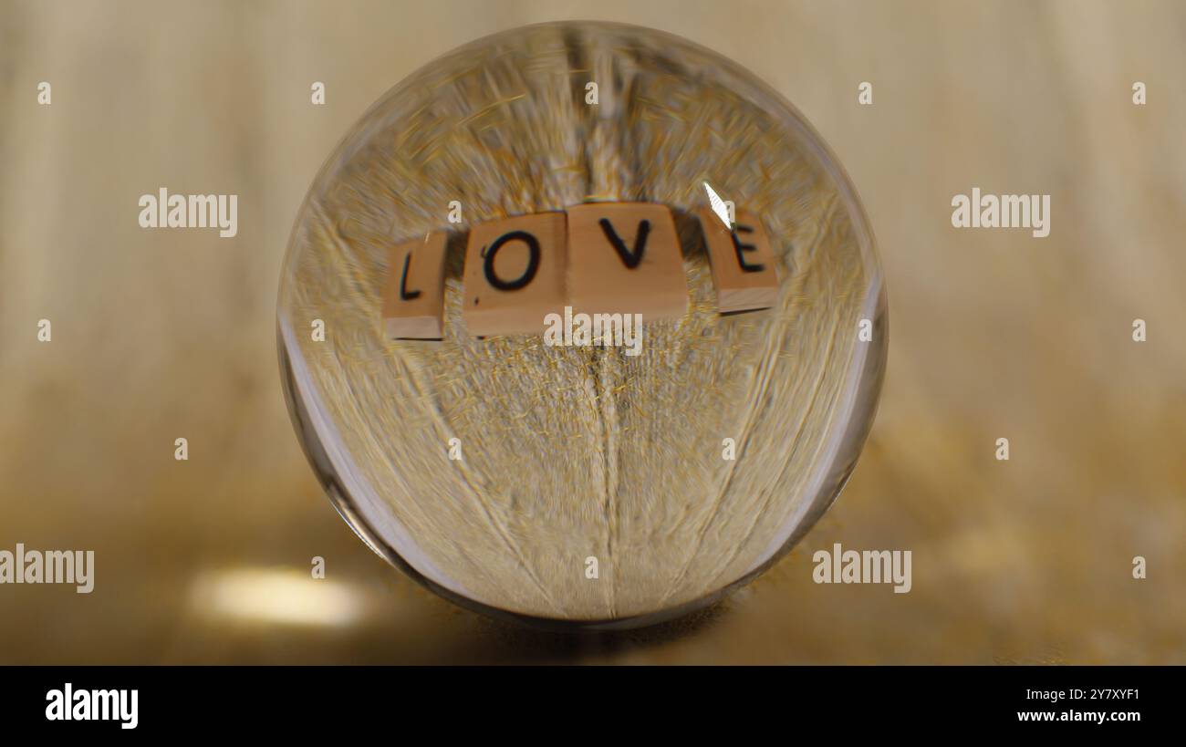 Primo piano di una sfera di vetro che riflette una struttura gialla con la scritta Love Foto Stock