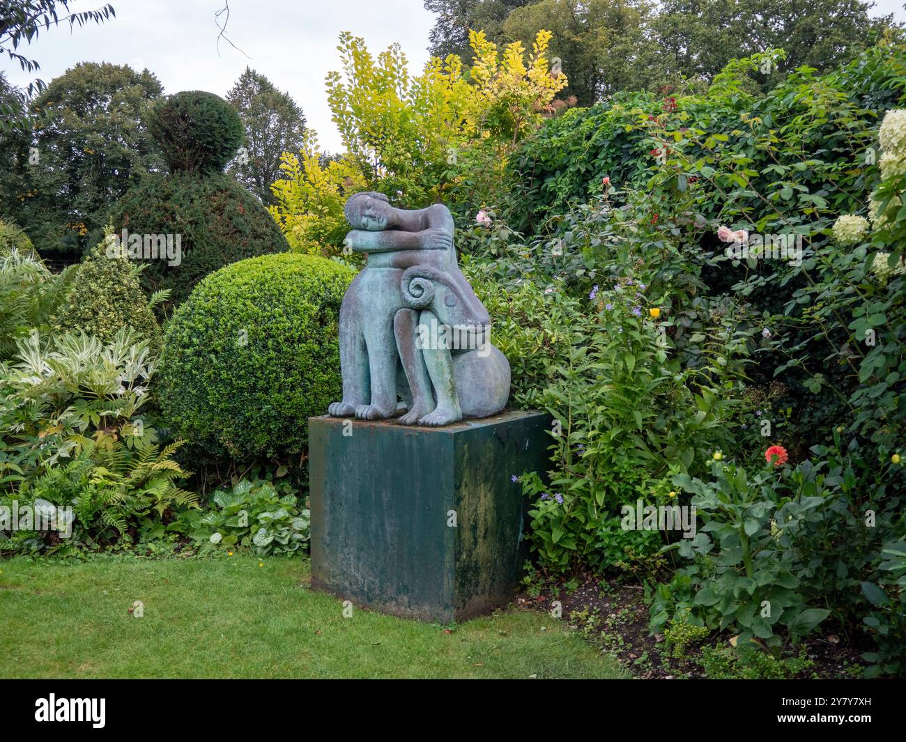 Chenies Manor Garden a settembre; angolo del giardino con sempreverde, arbusti, topiario e una scultura di una figura addormentata e ariete. Foto Stock