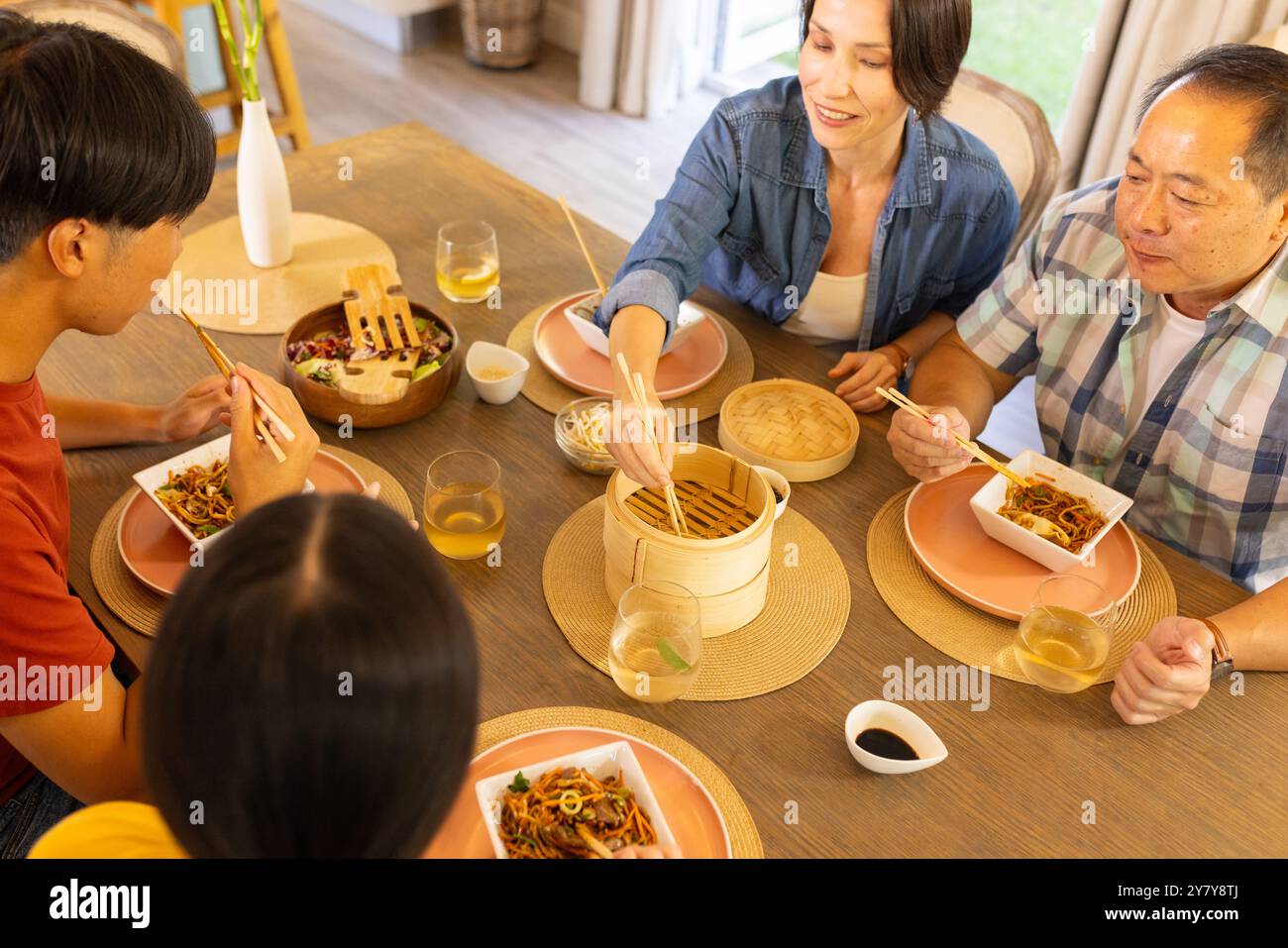 A casa, la famiglia asiatica si diverte a mangiare insieme, mangiando spaghetti con bacchette al tavolo da pranzo Foto Stock