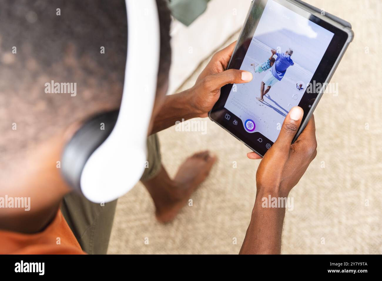 Utilizzando un tablet e indossando le cuffie, l'uomo che modifica foto di una spiaggia Foto Stock