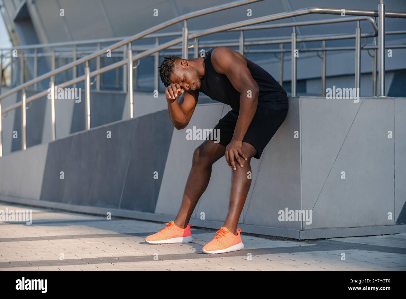 L'intera lunghezza dell'uomo africano stanco in abbigliamento sportivo riposa dopo un allenamento sportivo all'aperto Foto Stock