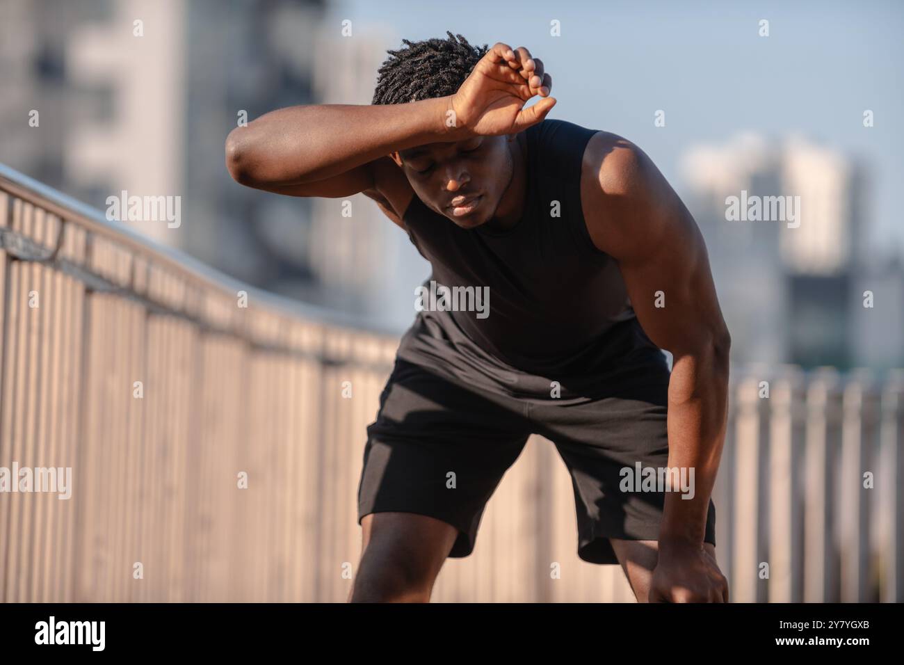 Giovane atleta africano che copre il viso con la mano e si prende cura della stanchezza dopo gli allenamenti sportivi all'aperto Foto Stock