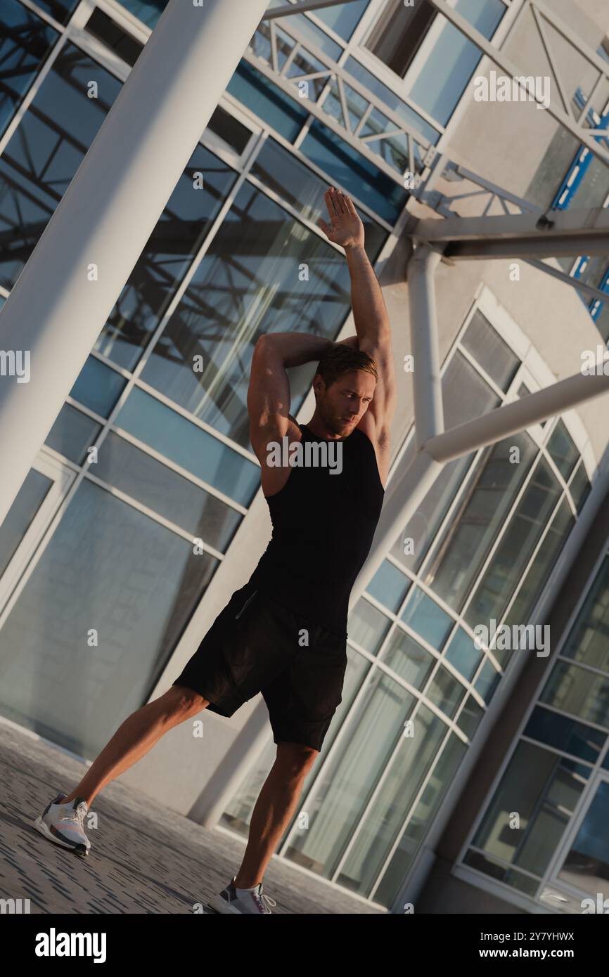 Bel muscoloso in abbigliamento sportivo che fa esercizi di stretching all'aperto la mattina presto Foto Stock