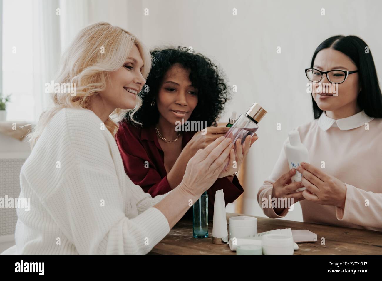 Tre donne mature che esaminano trattamenti di bellezza sedute alla scrivania insieme Foto Stock