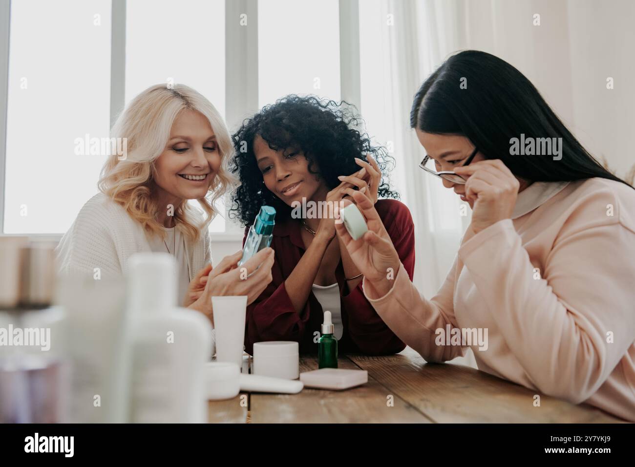Tre donne mature che esaminano i prodotti di bellezza sedute alla scrivania insieme Foto Stock