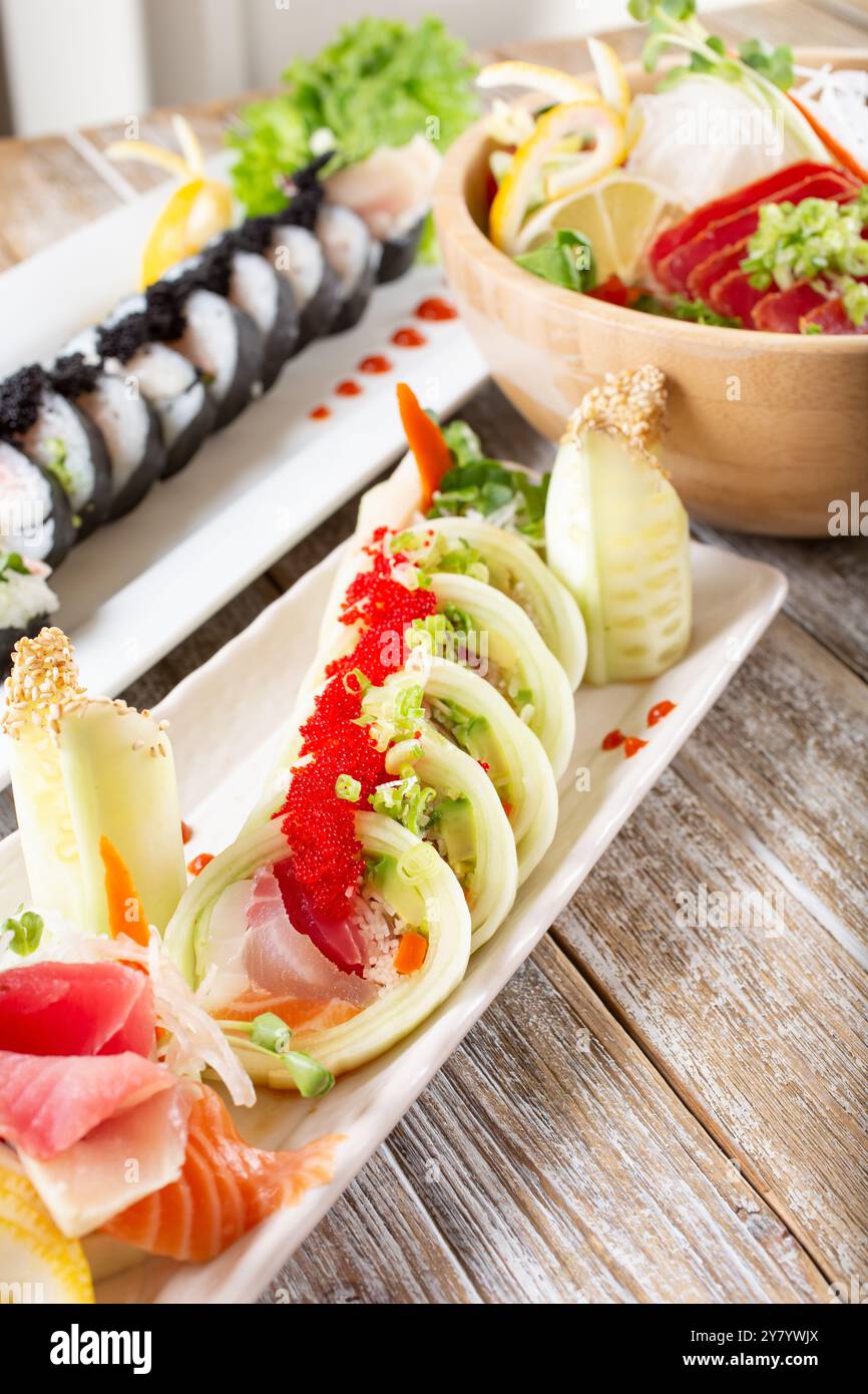 Una vista di un sushi roll caratterizzato da cetriolo come involtino, oltre ad una varietà di altri piatti di sushi e pesce su un tavolo. Foto Stock