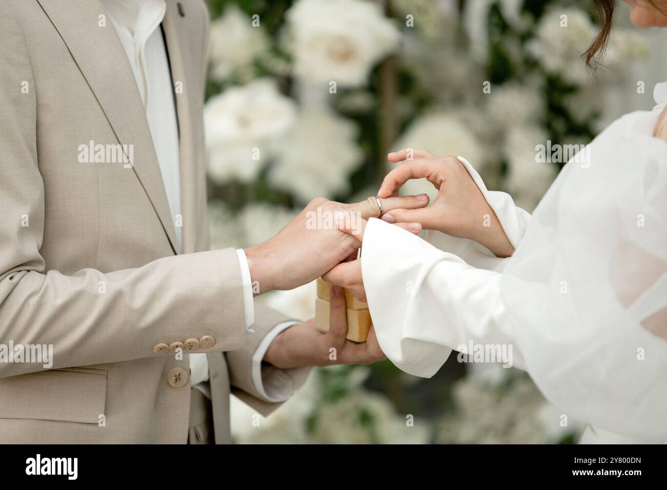 Una coppia si riunisce in un meraviglioso ambiente floreale, scambiandosi anelli per esprimere i propri voti di amore e collaborazione, catturando un momento di sincero Foto Stock