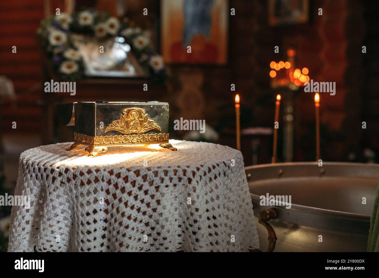 Una scatola dorata con dettagli intricati si trova su una tovaglia in pizzo bianco, illuminata da una luce soffusa. Candele alte bruciano sullo sfondo, lanciando una guerra Foto Stock