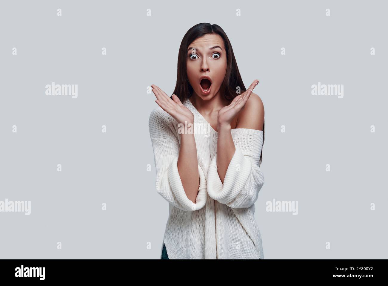 Oh mio Dio! La giovane donna scioccata tiene la bocca aperta mentre si trova su uno sfondo grigio Foto Stock