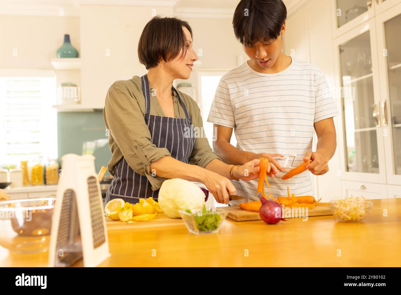 Cucinare in cucina, la madre e il figlio adolescente preparano le verdure, unendosi alla preparazione dei pasti Foto Stock