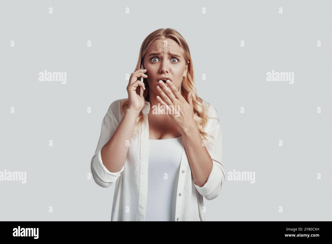 Una giovane donna frustrata che parla con lo smartphone e fa un volto mentre si trova su uno sfondo grigio Foto Stock Una giovane donna frustrata che parla con lo smartphone e fa un volto mentre si trova su uno sfondo grigio Foto Stock