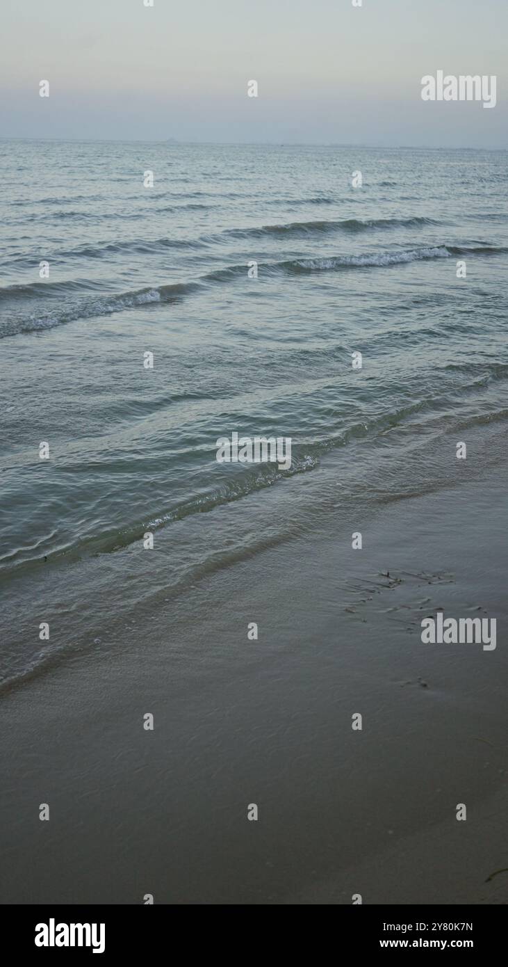 Tranquilla passeggiata sul mare con onde dolci e spiaggia sabbiosa al crepuscolo. Foto Stock