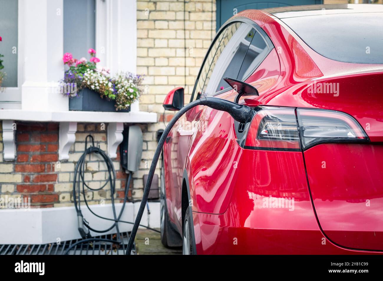 Auto elettrica ricaricata fuori casa in un tipico ambiente residenziale di periferia britannica Foto Stock