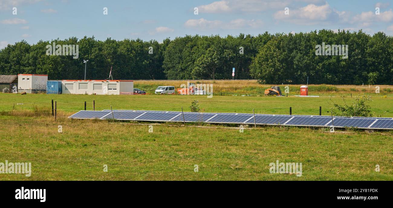 cantiere per una fattoria a energia solare alla luce del sole vicino a un'autostrada, con alberi e cieli blu. Impianto su piccola scala nel terreno. Foto Stock