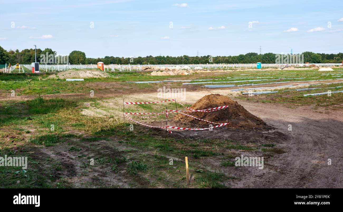 sito di costruzione di una fattoria solare, posto contro un cielo limpido. I terreni agricoli sono utilizzati per la produzione di energia rinnovabile. Foto Stock