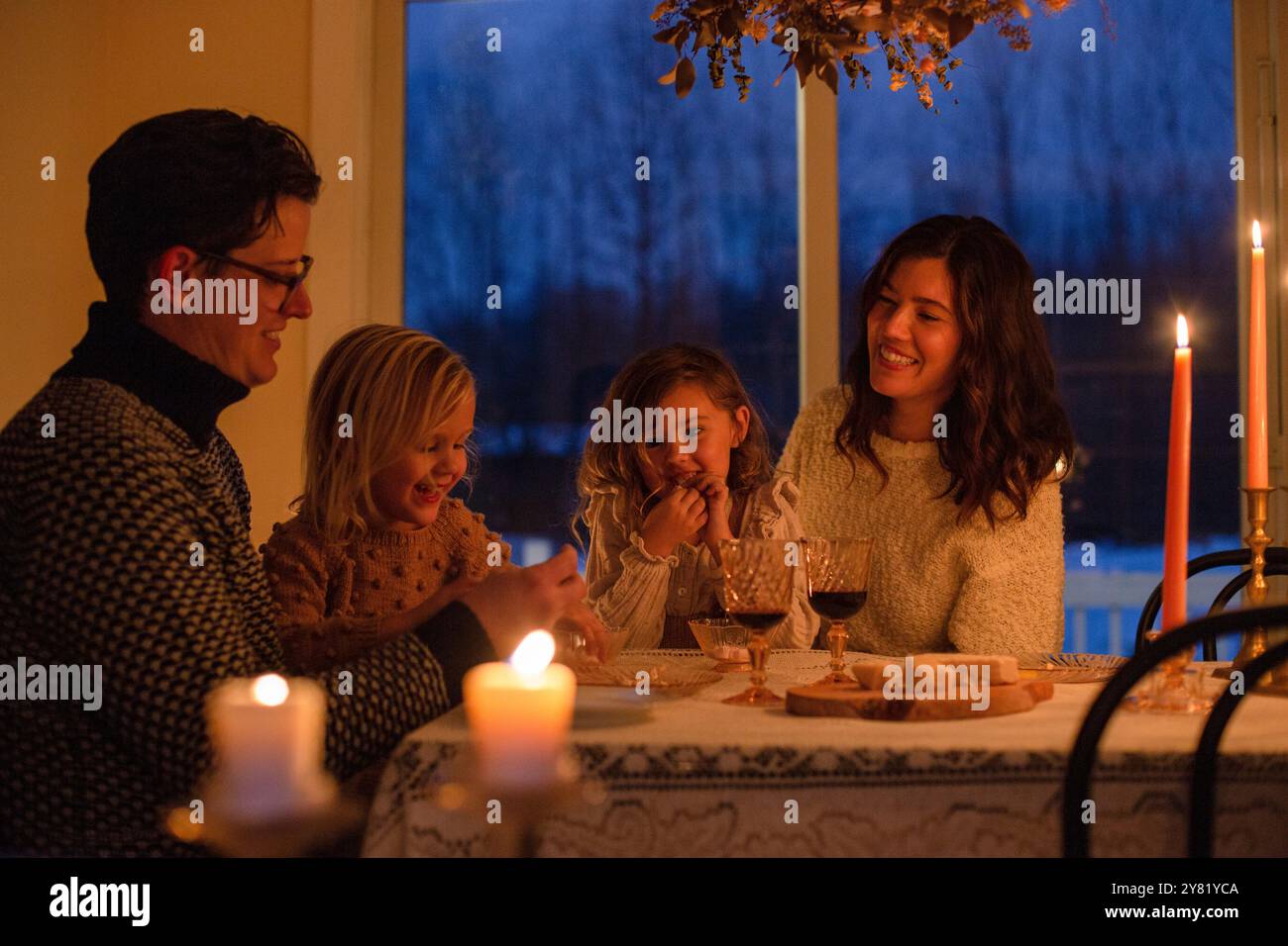 La famiglia può gustare insieme una cena a lume di candela, sorridendo e condividendo un momento di gioia intorno a un tavolo. Foto Stock