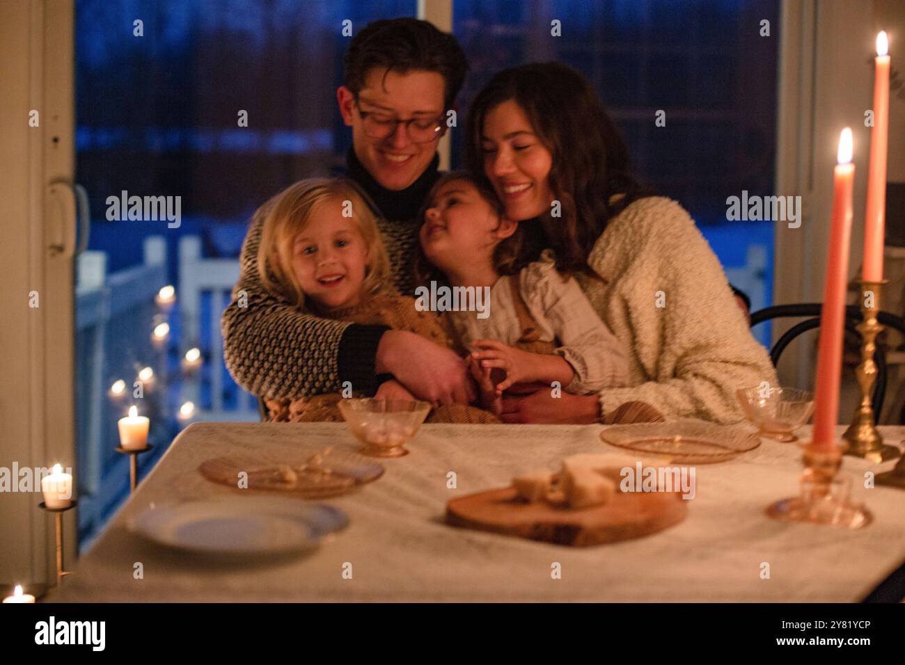 Una famiglia gode di un'accogliente cena a lume di candela, sorridente e abbracciata con amore e calore. Foto Stock