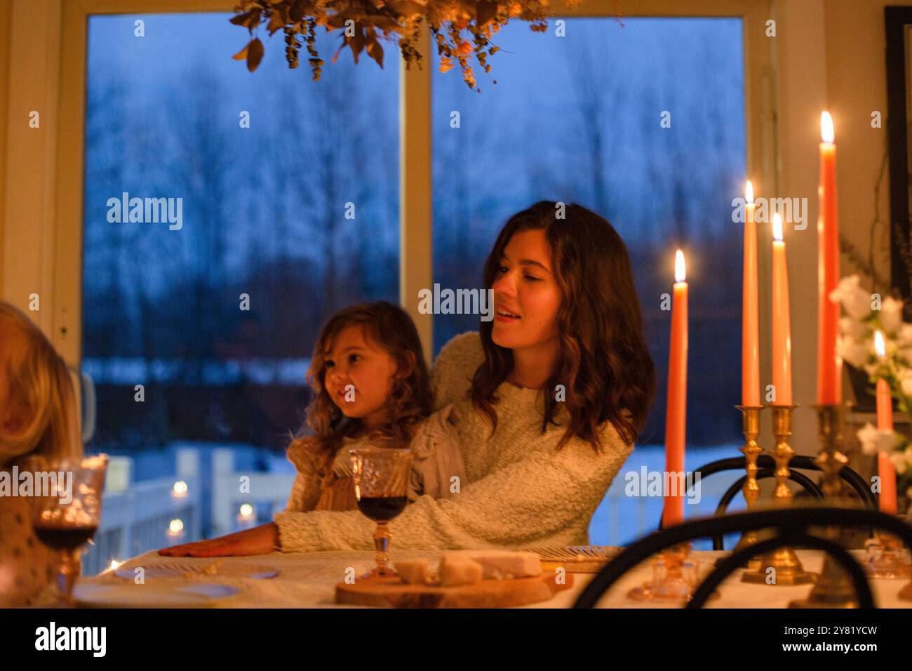 Una famiglia gode di una cena intima a lume di candela con una vista del cielo crepuscolo attraverso la finestra. Foto Stock