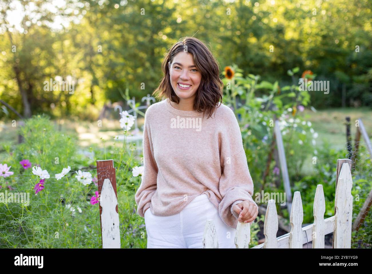 Donna sorridente in un giardino con una recinzione in legno e fiori sullo sfondo. Foto Stock