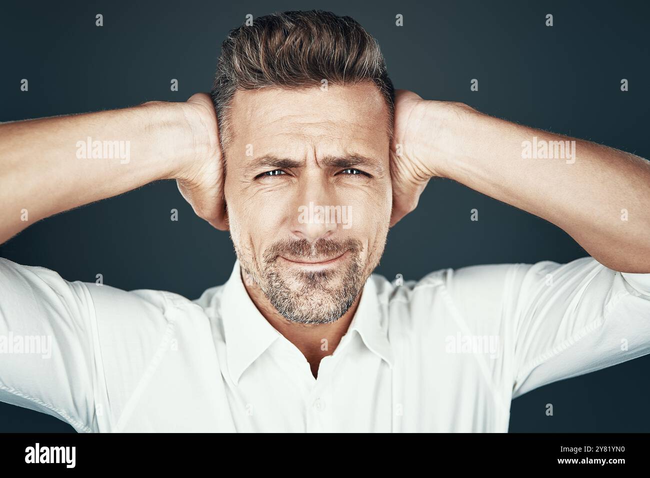 Oh no! Un giovane frustrato che copre le orecchie con le mani e crea un volto mentre si sta in piedi su sfondo grigio Foto Stock Oh no! Un giovane frustrato che copre le orecchie con le mani e crea un volto mentre si sta in piedi su sfondo grigio Foto Stock