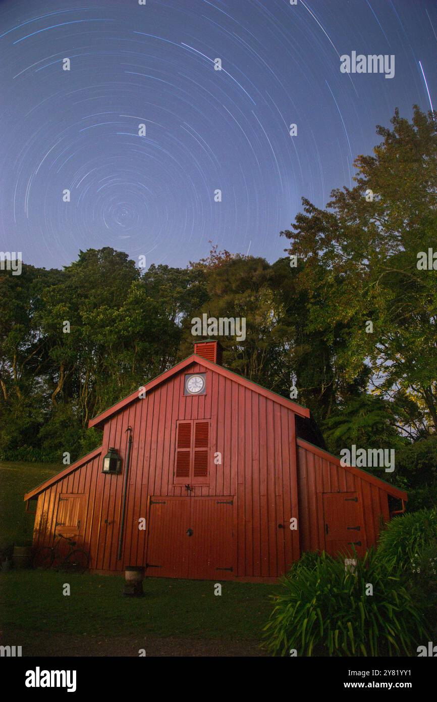 I sentieri delle stelle si snodano sopra un cottage di legno rosso durante una lunga sessione fotografica notturna a Auckland, nuova Zelanda Foto Stock