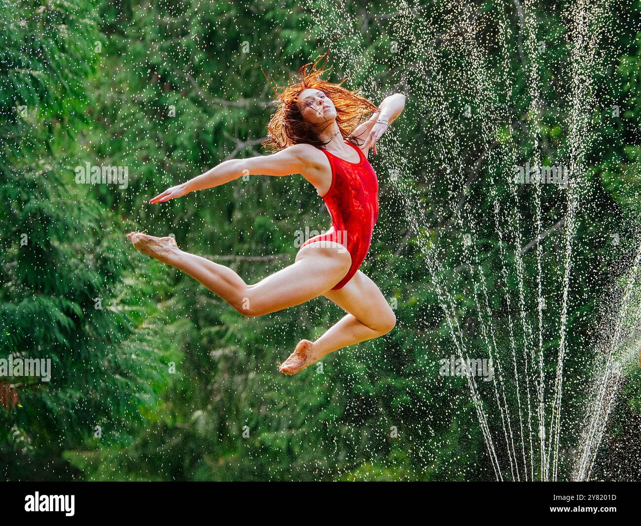 Giovane donna con un lembo rosso che esegue un'elegante danza a mezz'aria sullo sfondo di spruzzi d'acqua. Foto Stock