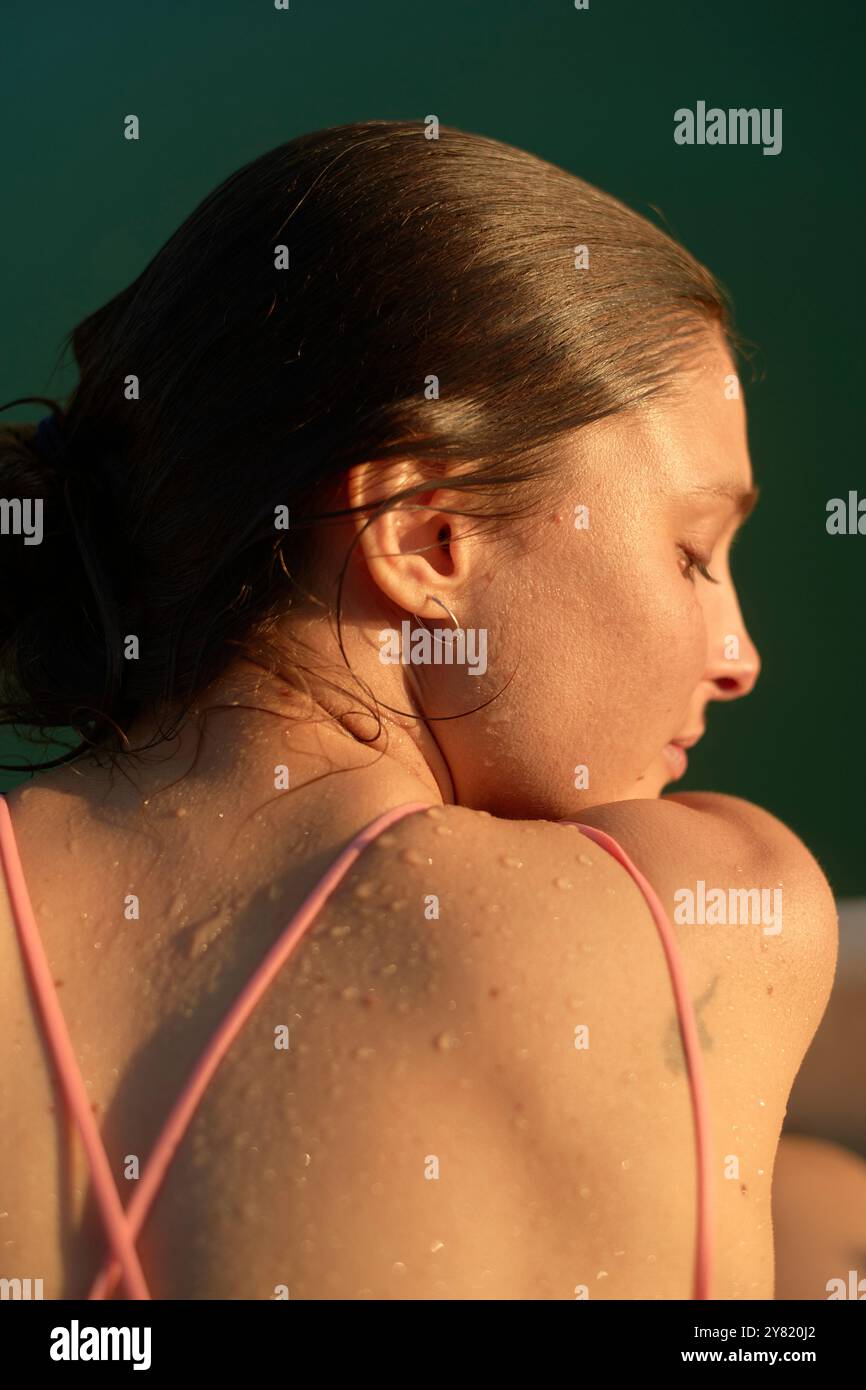 Profilo laterale di una giovane donna con pelle bagnata su sfondo verde. Foto Stock