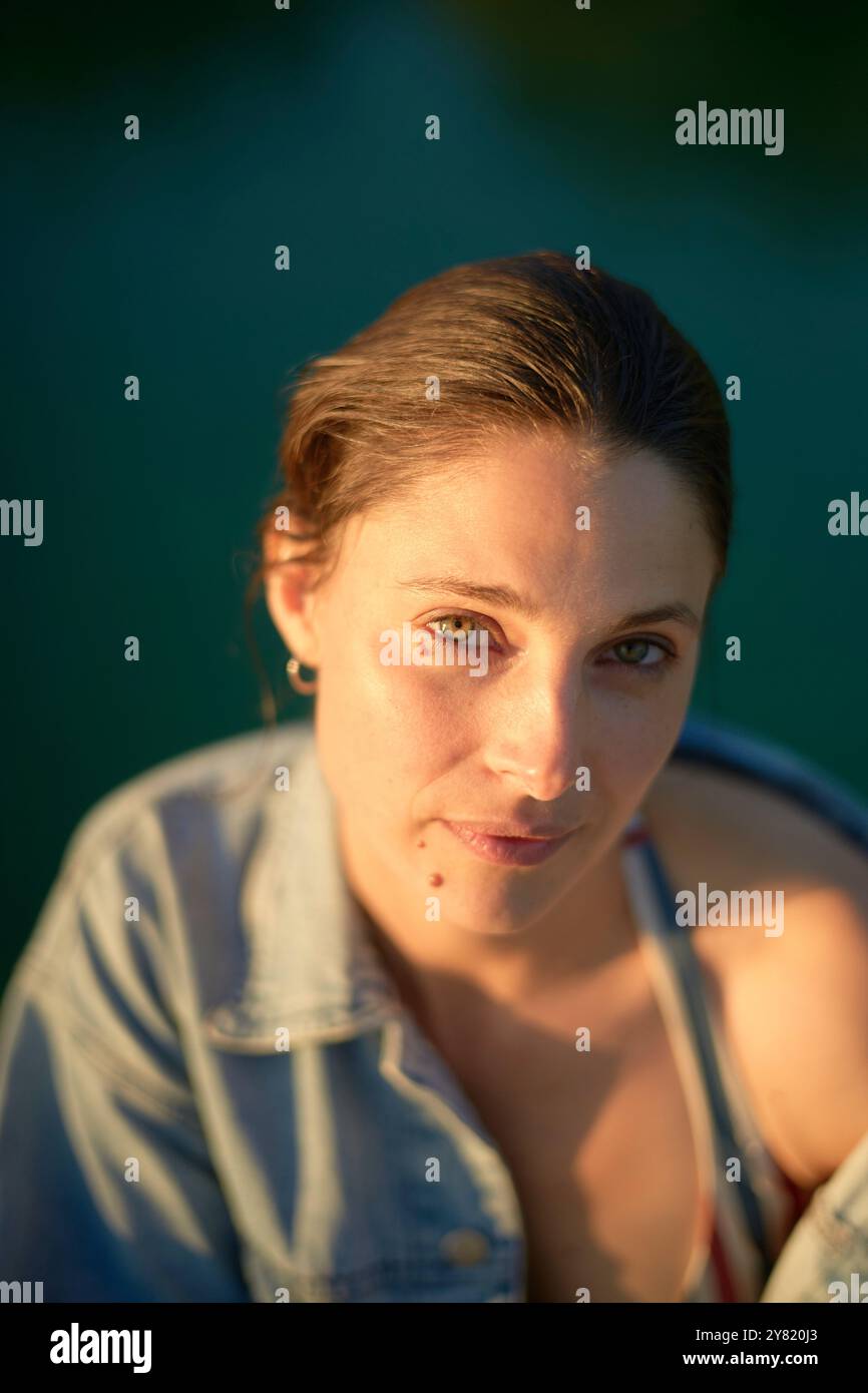 Ritratto di una donna con i capelli marroni in una camicia in denim inondata dalla luce soffusa del sole Foto Stock