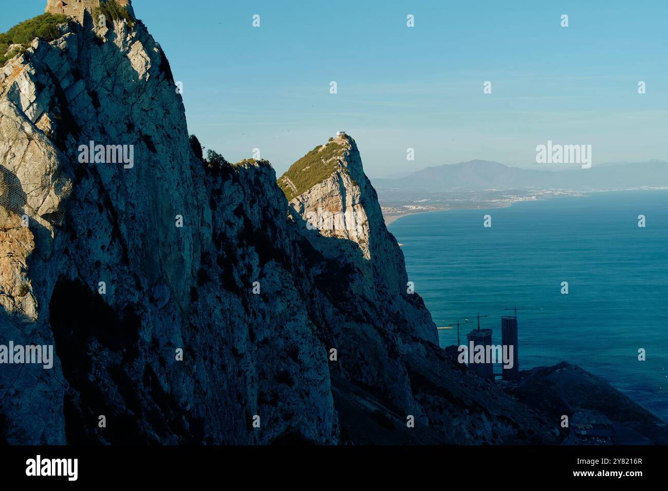 Vista sull'oceano su scogliere ripide con edifici lontani sotto un cielo azzurro. Foto Stock