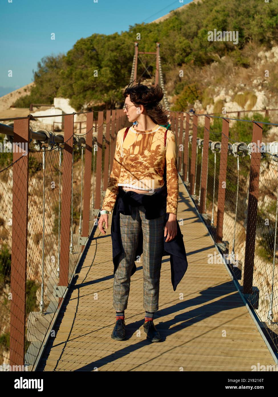 Donna in abbigliamento casual si erge su un ponte sospeso che si affaccia su una vista panoramica. Foto Stock