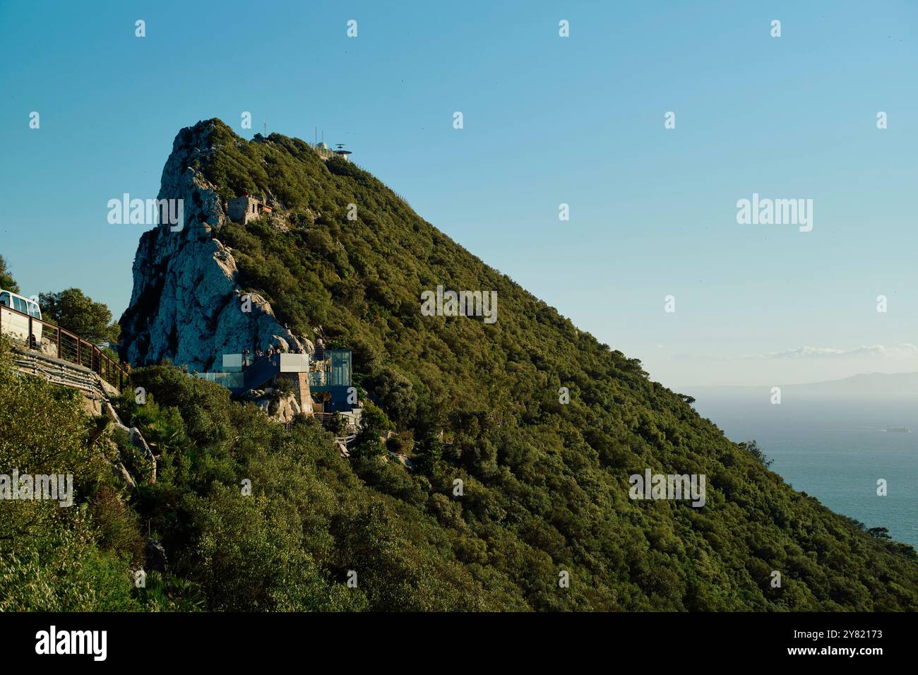 Collina verde con un picco roccioso ed edifici sotto un cielo azzurro. Foto Stock
