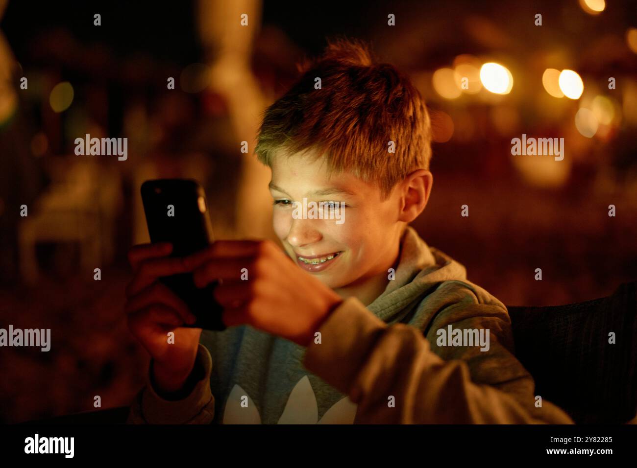 Ragazzo sorridente che usa lo smartphone con calde luci luminose sullo sfondo. Foto Stock